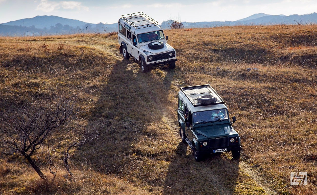 Two Land Rover Defenders driving down a grassy hill