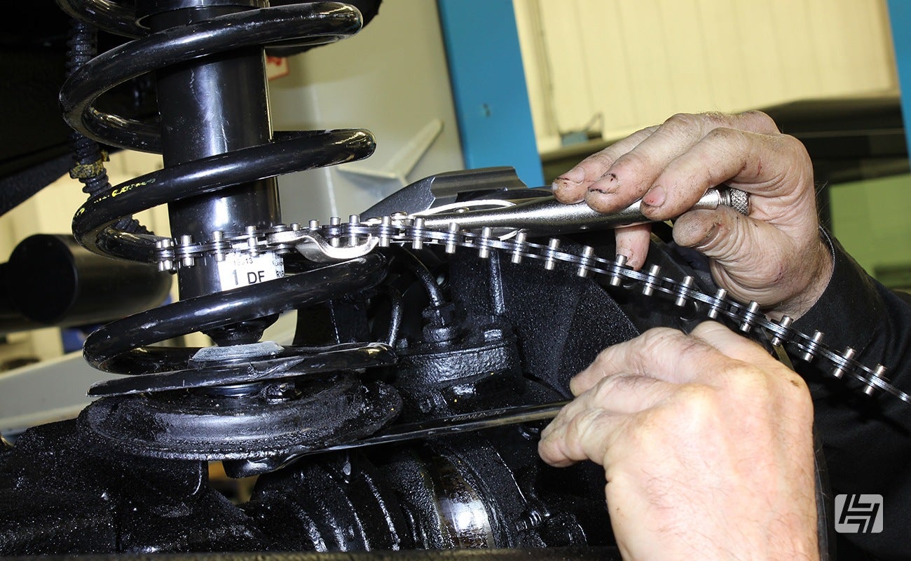 mechanic uses a chain device to hold a shock absorber still 