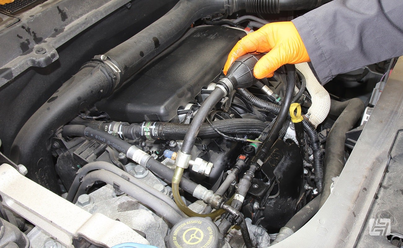 Mechanic using hand pump to prime the new fuel filter on Land Rover Freelander 2 TD4