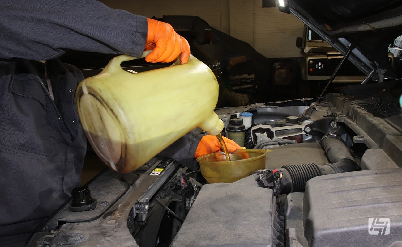 Mechanic filling up the oil on Land Rover TD4 engine using a jug and funnel