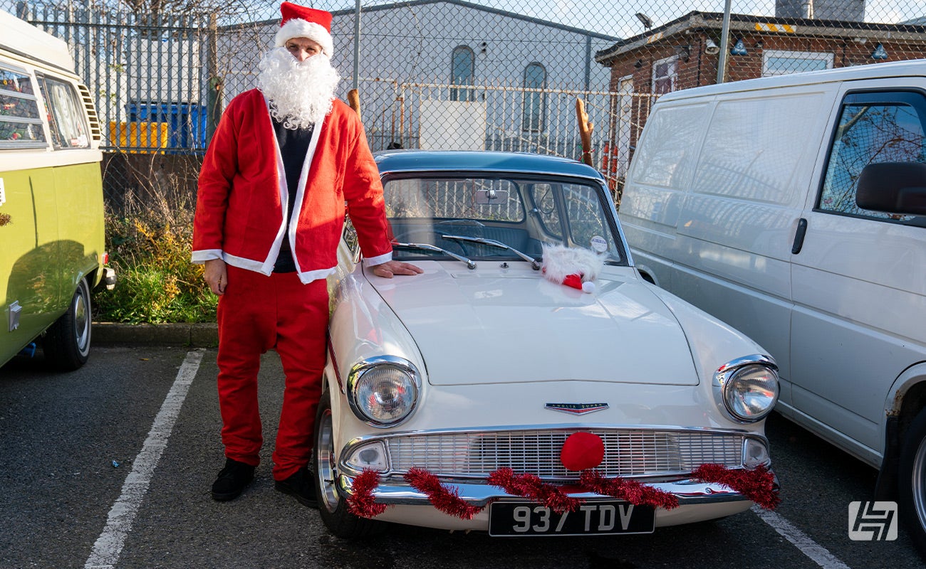 Classic Ford Anglia decorated with red tinsel and owner dressed as Father Christmas