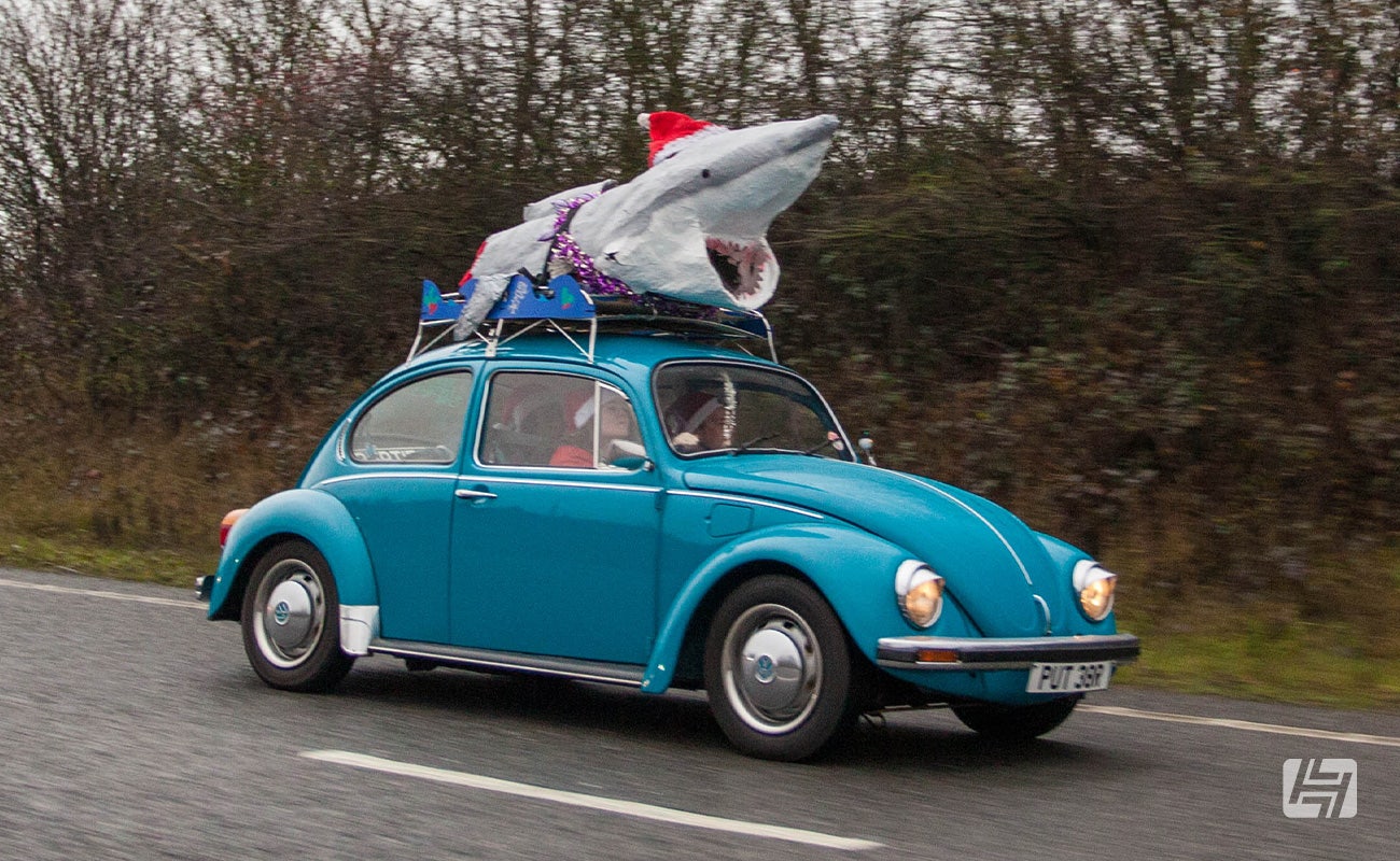 Blue VW Beetle with large shark on the roof rack