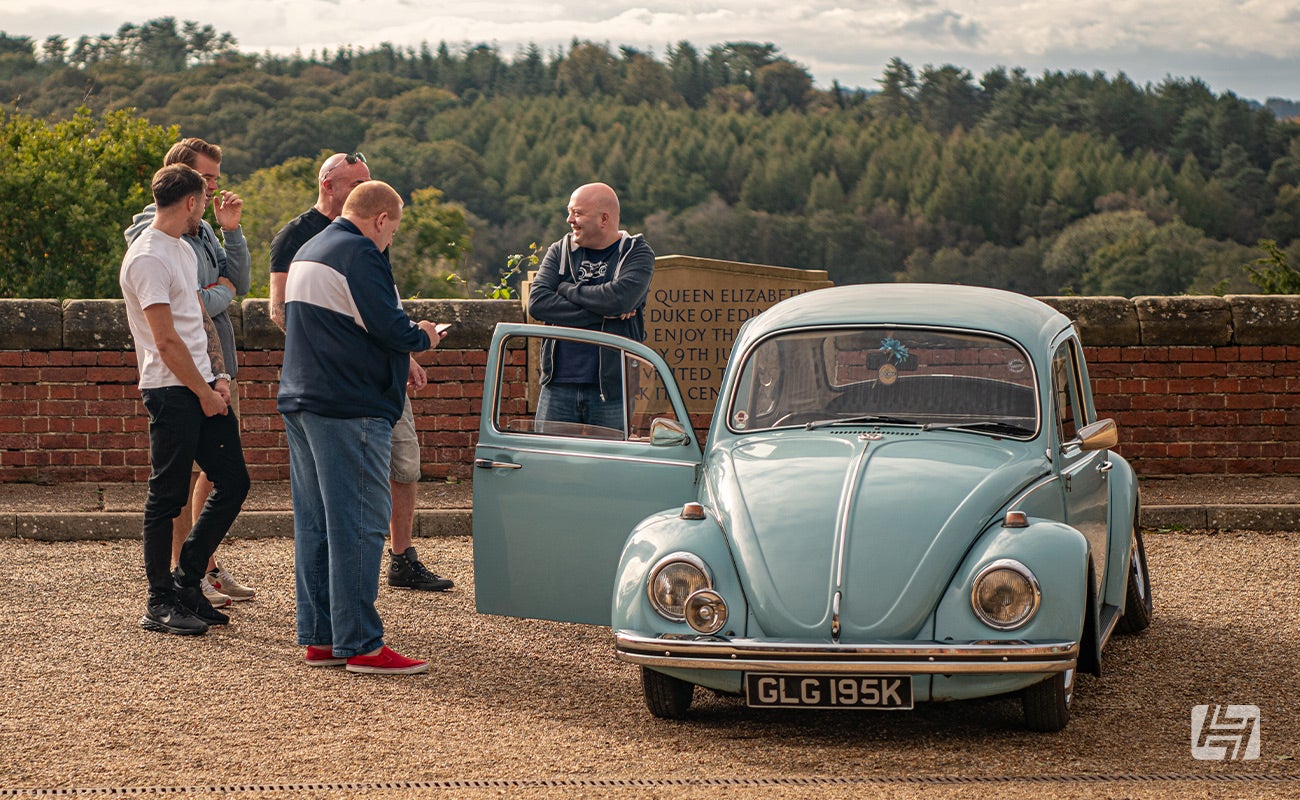 VW enthusiasts chatting by blue VW Beetle at Heritage Parts Centre photoshoot Ardingly 2023