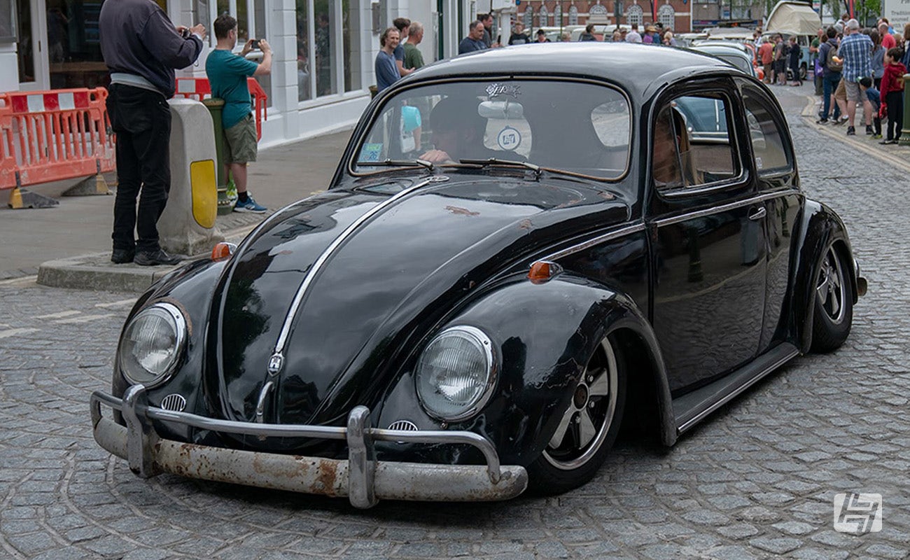 Slammed black VW Beetle on polished Fuchs wheels driving at Plum Jam event in Horsham, West Sussex