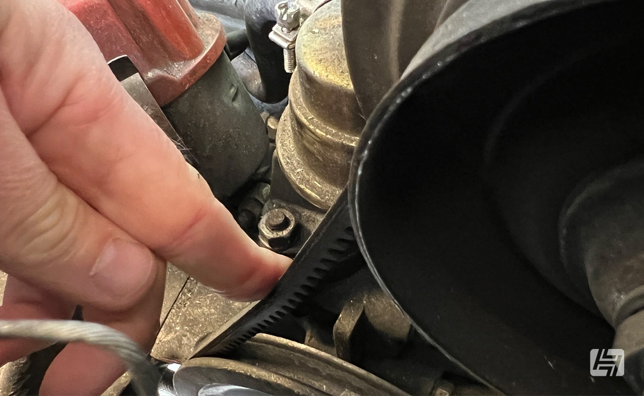 Pushing a fan belt with your finger to test deflection and tightness