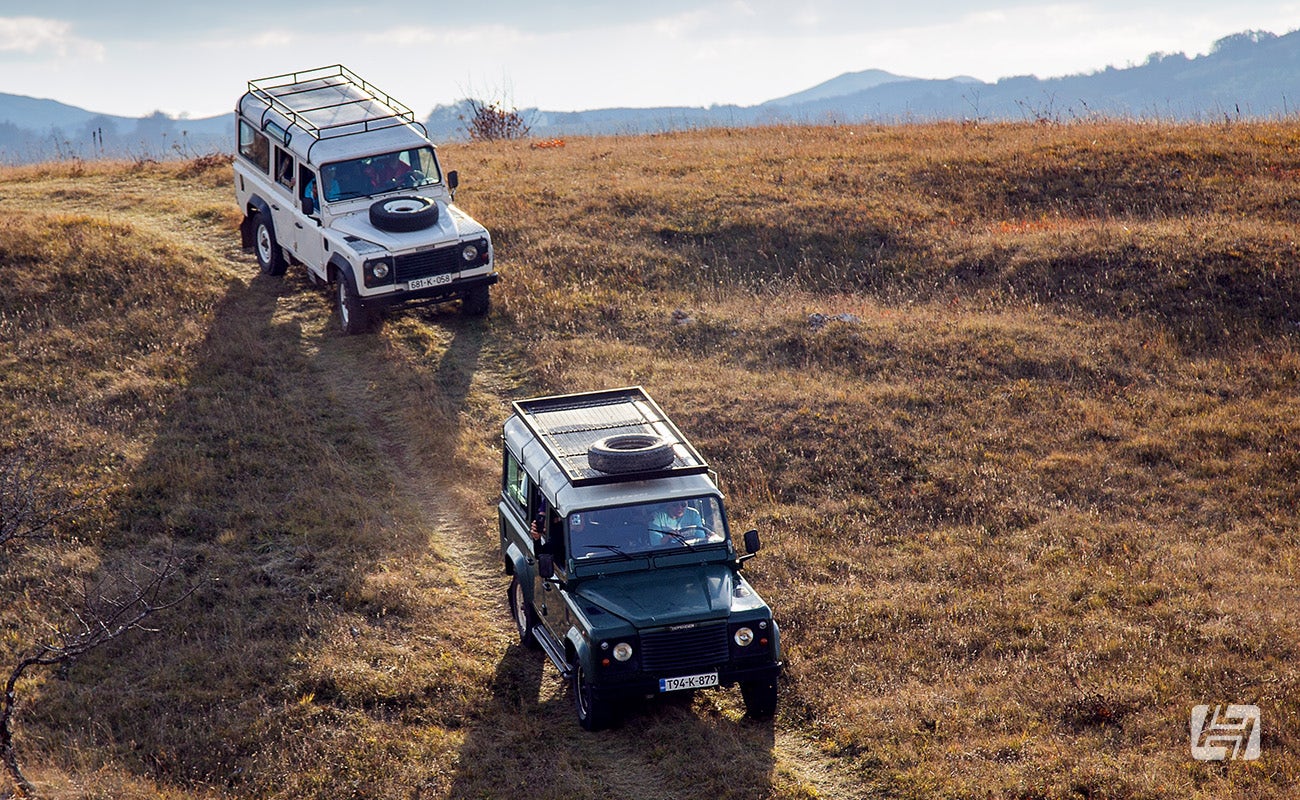 Two Land Rovers driving off road down a grassy hill